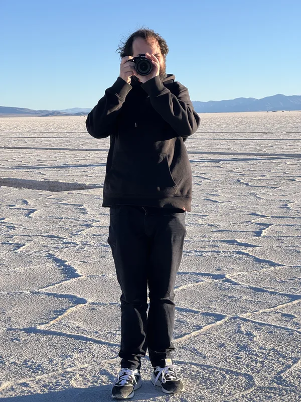 A photographer, dressed entirely in black, standing in the middle of a salt flat — most likely the Black Rock Desert pla