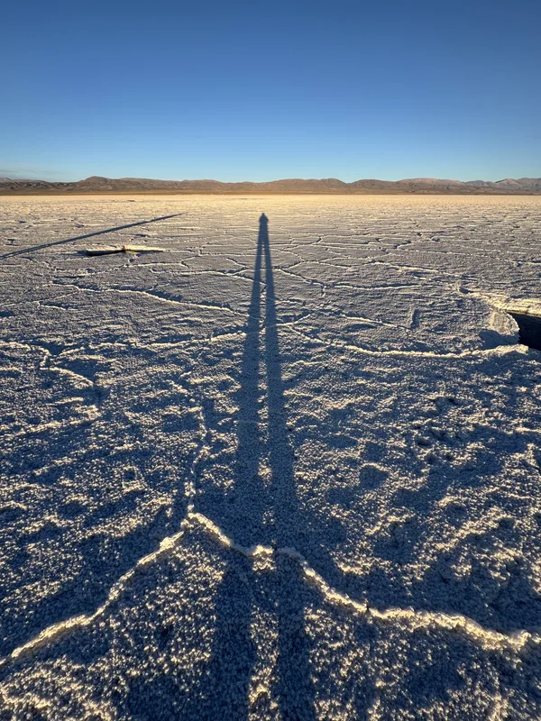 The photographer's shadow cast across a salt flat — likely the Salar de Uyuni or a similar Argentine/Bolivian salt plain