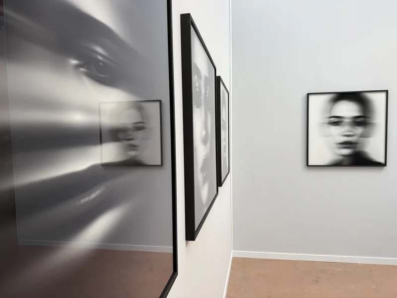 A gallery installation of large-format black-and-white portrait photographs, depicting blurred or multiplied human faces