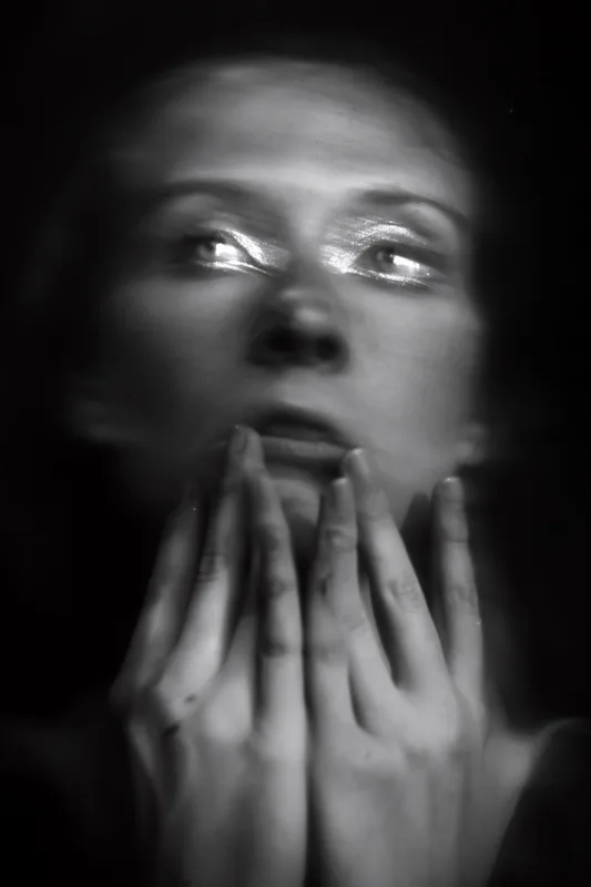 A woman pressing her hands together against her face, her eyes directed upward and to the side