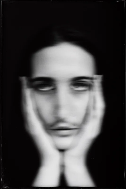 A young person, gender ambiguous, face cradled in their own hands, identity fragmented by double exposure or motion acro