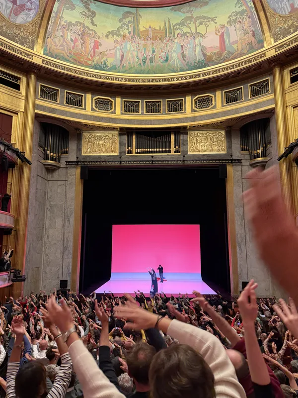 Mid-ovation. The performers miniaturized. The audience becomes the event.