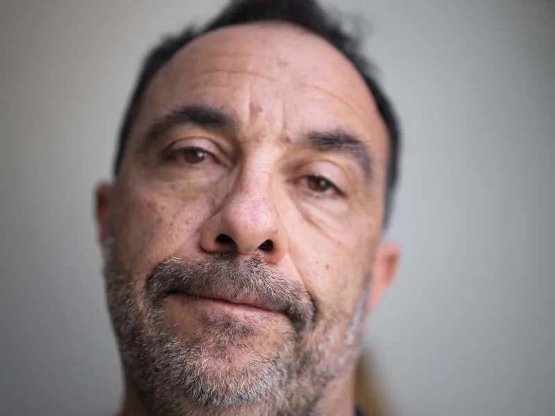 A middle-aged man, Mediterranean or Middle Eastern complexion, salt-and-pepper stubble, dark eyes, prominent horizontal 