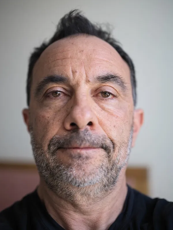 A middle-aged Mediterranean or Southern European man, mid-fifties, in a black garment, facing the camera directly in an 