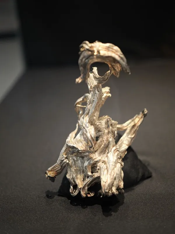 A small-scale sculptural object — likely cast metal or silvered organic material — presented as a gallery artifact on a 