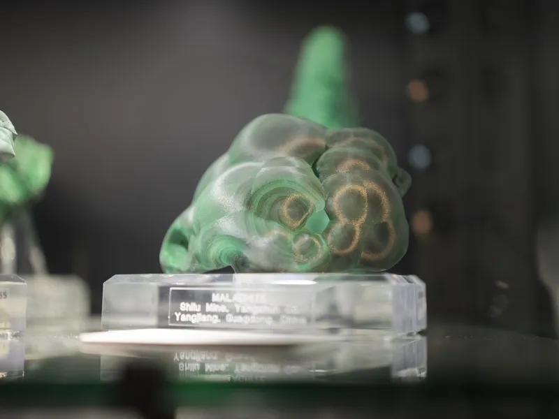 A polished botryoidal malachite specimen on an acrylic museum display base, labeled from the Shilu Mine, Yangchun, Guang
