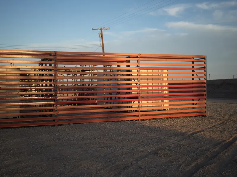 A horizontal steel slat border fence, likely the US-Mexico border wall or a similar infrastructural barrier, photographe
