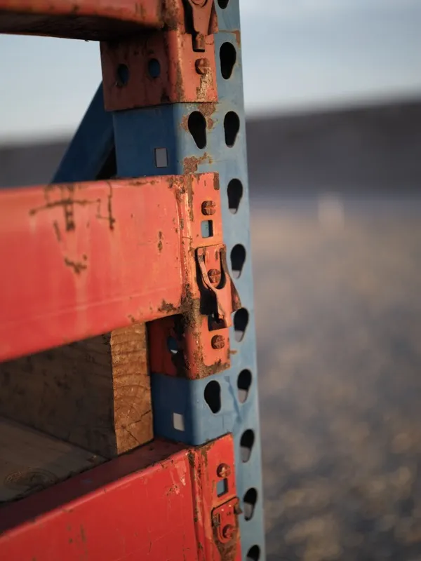 The connection joint of a weathered industrial pallet racking system, photographed in an outdoor or semi-outdoor environ