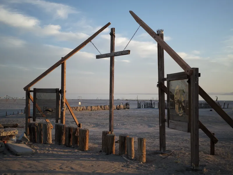 A skeletal wooden installation structure on the Salton Sea shoreline — almost certainly in the Bombay Beach or East Jesu