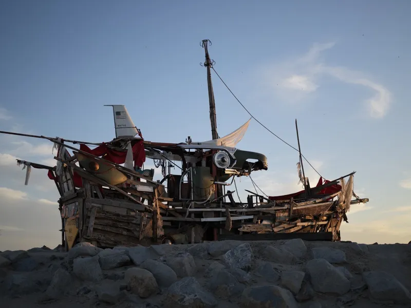 A large-scale assemblage sculpture constructed from salvaged wood, red fabric, rope, and the fuselage of a small aircraf