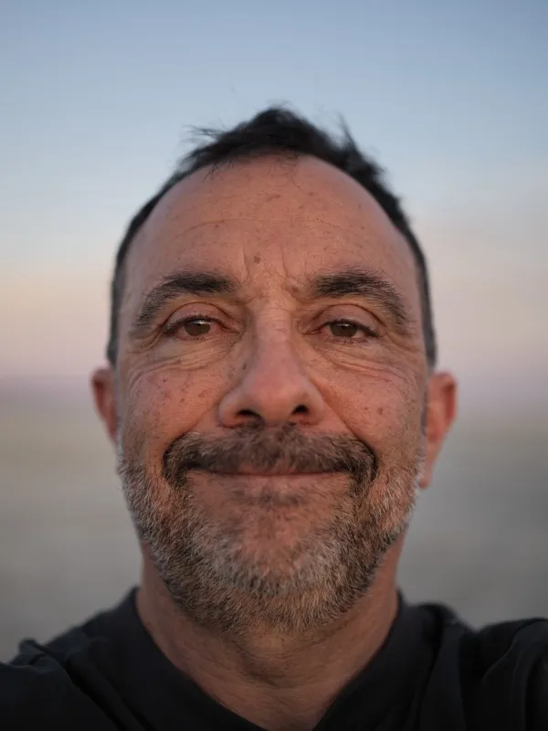 A middle-aged man of Mediterranean or Middle Eastern appearance, salt-and-pepper stubble, weathered skin texture, a smal