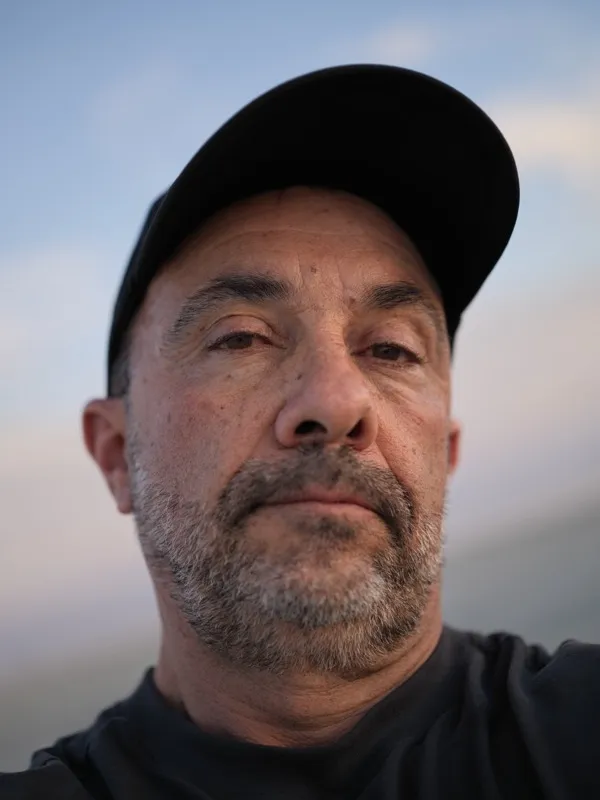 A middle-aged man, Mediterranean or Middle Eastern features, wearing a black baseball cap and black t-shirt