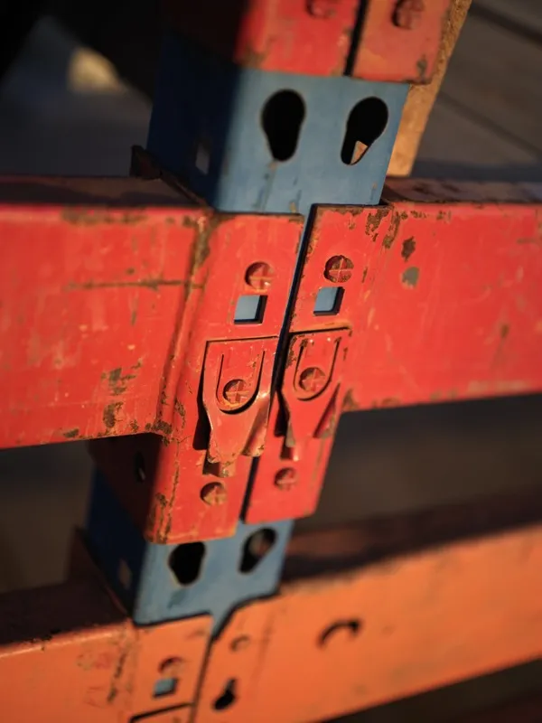 The locking connector joint between a blue steel upright and a red horizontal beam of industrial pallet racking, seen in