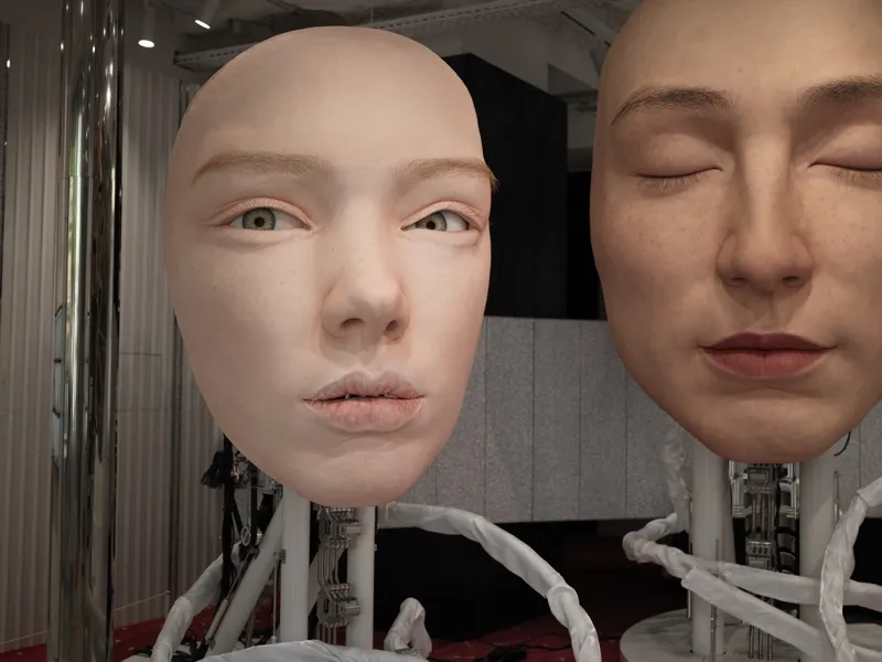 Two humanoid android heads mounted on mechanical neck assemblies, displayed in what appears to be a technology exhibitio