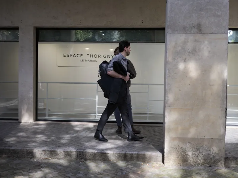 Two people — appearing to walk in close physical synchrony, possibly a couple — passing in front of the Espace Thorigny 