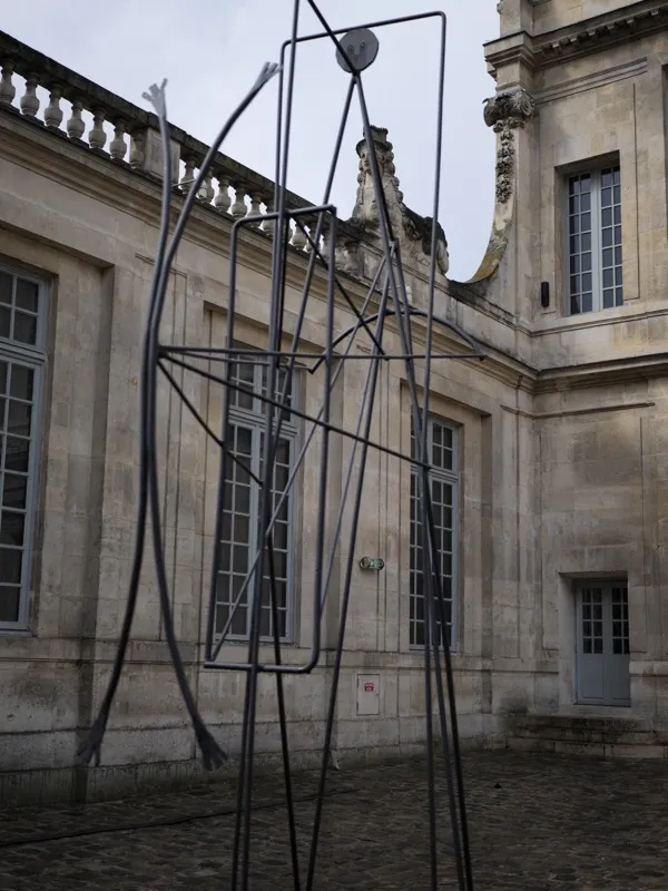 A large-scale wire or rod sculpture, anthropomorphic in its verticality, installed in the courtyard of a French neoclass