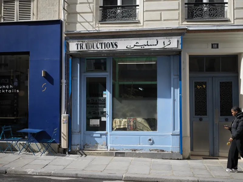 A bilingual French-Arabic translation services office on a Paris street, its facade worn and modest, its sign quietly en