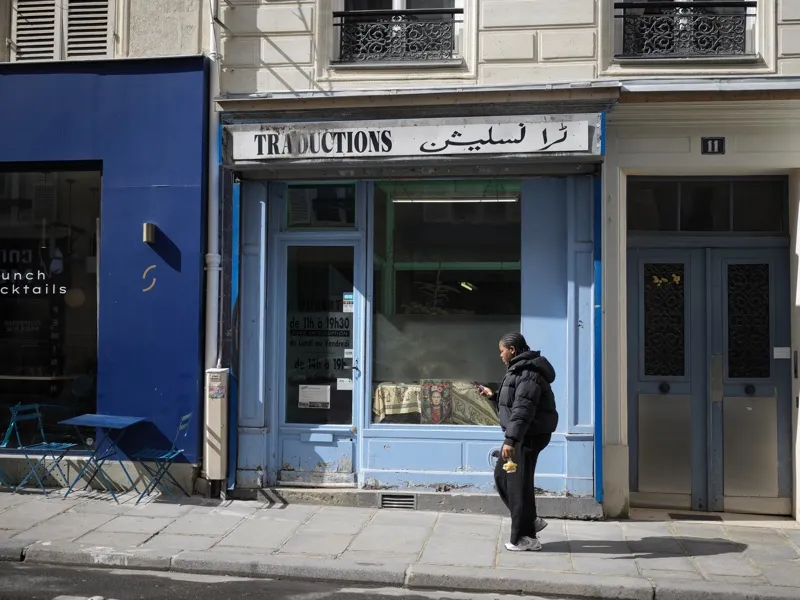 A translation bureau storefront — 'TRADUCTIONS' in French and Arabic — on a working-class Parisian street, with a solita