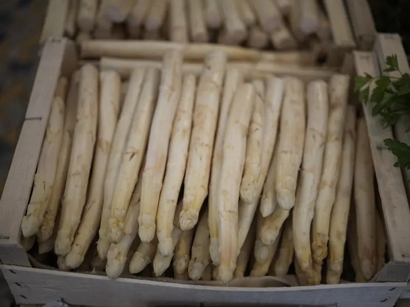 White asparagus spears packed in wooden market crates, photographed at an early morning market.