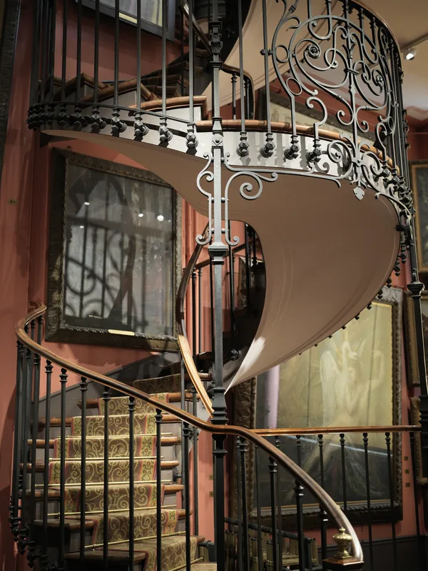 A wrought iron and wood spiral staircase, photographed in what appears to be a 19th-century interior or museum reconstru