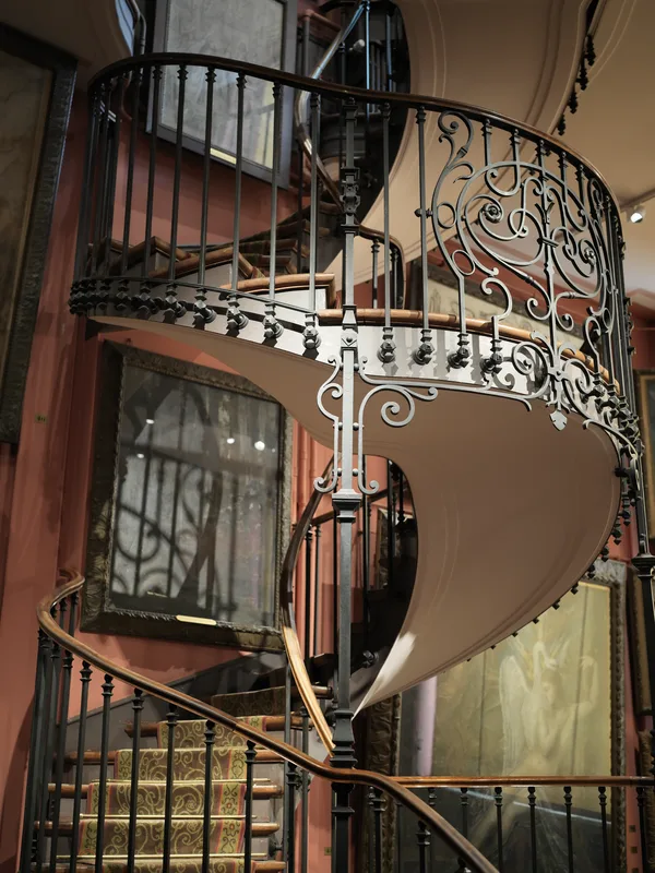 An ornate iron-and-wood spiral staircase inside what appears to be the Musée Gustave Moreau in Paris, based on the chara