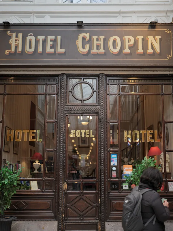 The ornate Art Nouveau façade of the Hôtel Chopin in Paris's Passage Jouffroy, with a lone pedestrian pausing before it