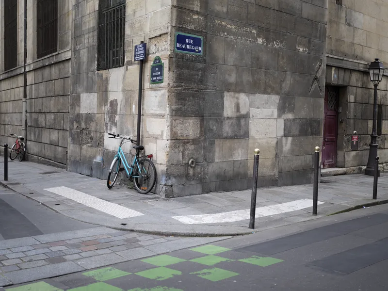 A teal utility bicycle leaned against the corner of a large cut-stone Haussmann-era building at Rue Beauregard, Paris, o