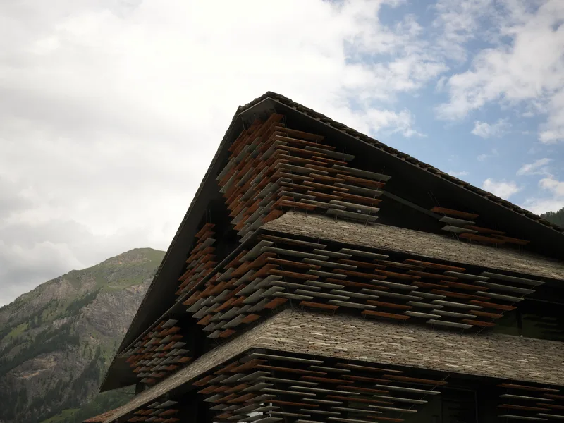 The overhanging corner of a contemporary building clad in alternating layers of slate and rusted steel or timber, photog