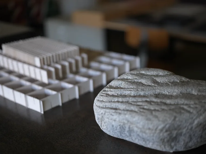 A rough stone and a white architectural scale model placed in proximity on a studio or desk surface